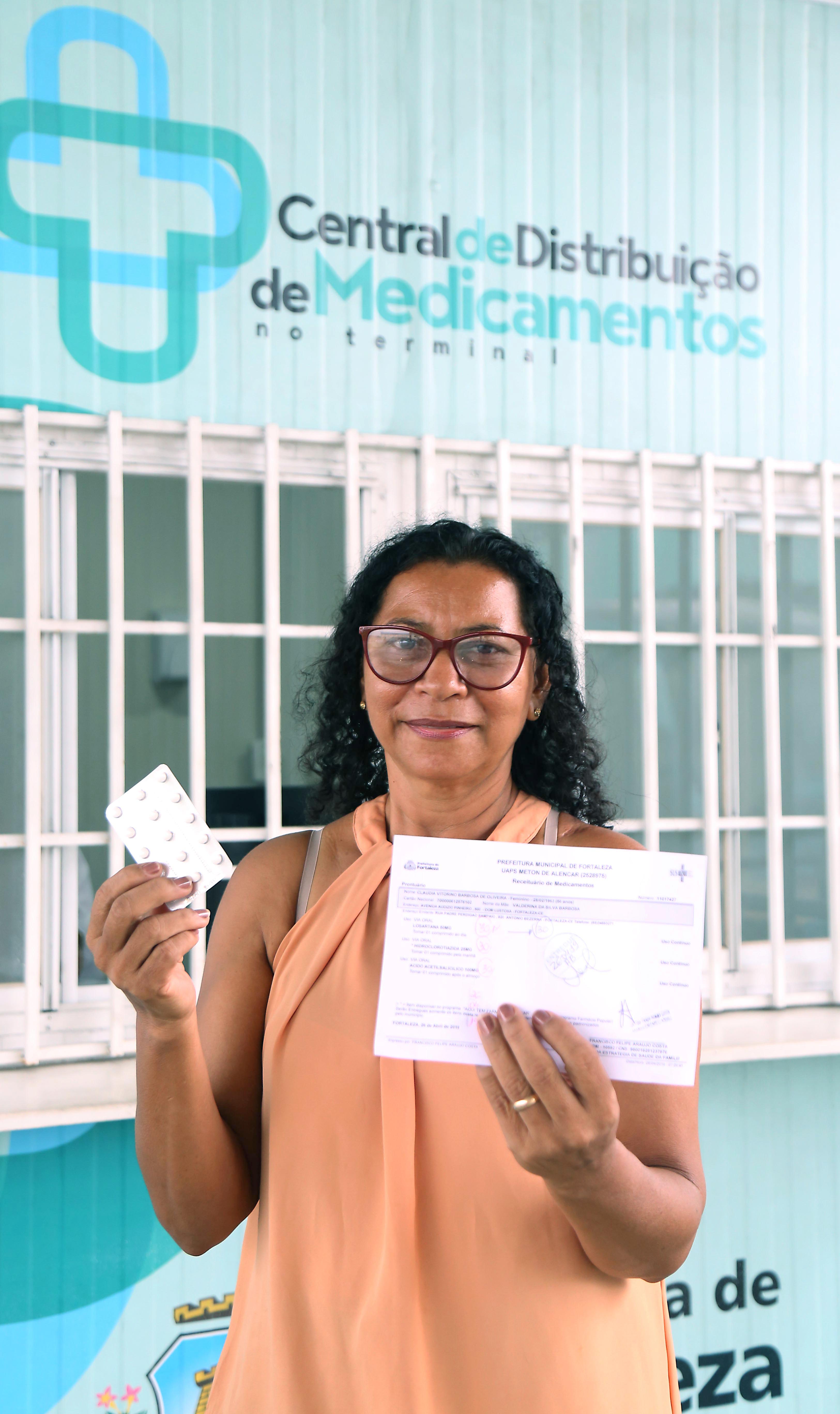 mulher mostra medicamento que retirou na Central