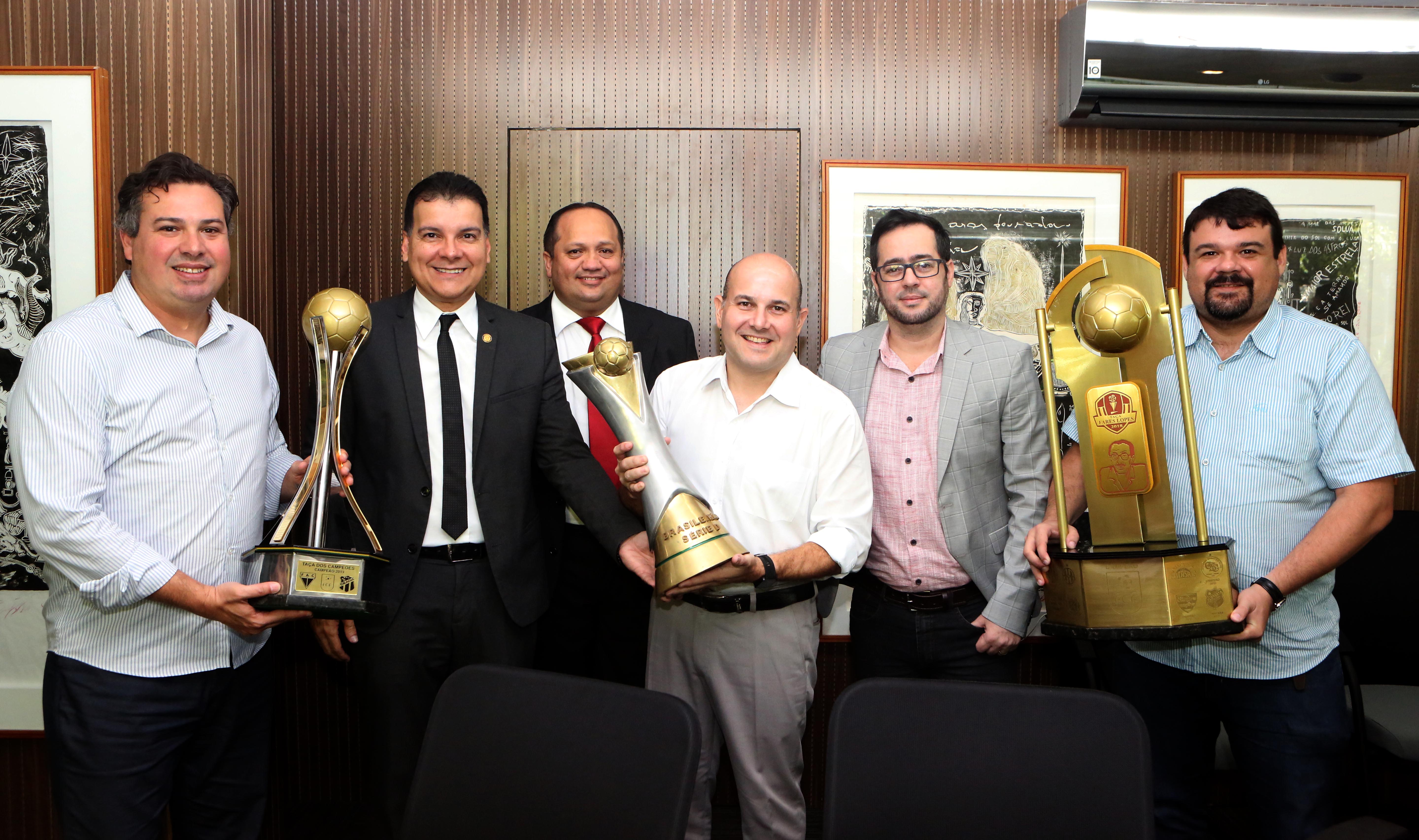 Homens em pé segurando troféus