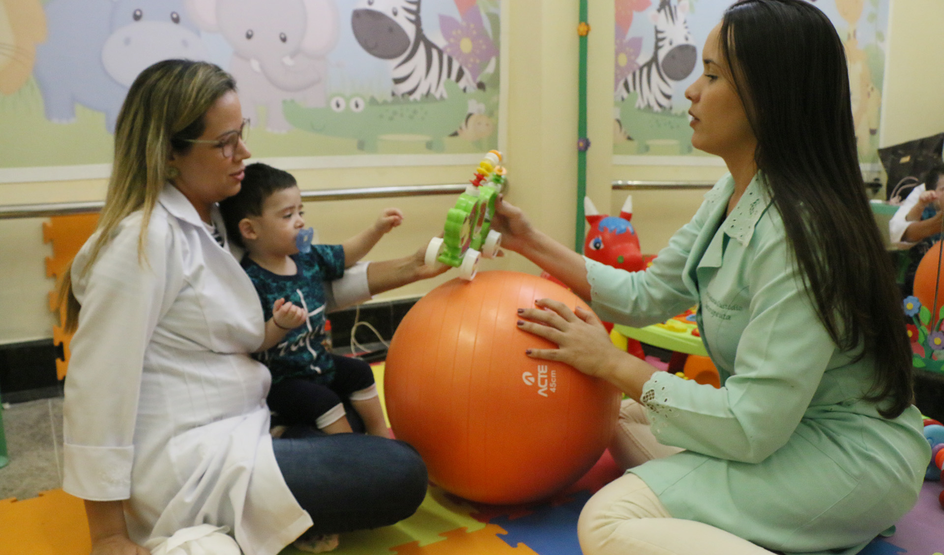 Duas mulheres de jaleco brincando com uma bola com criança