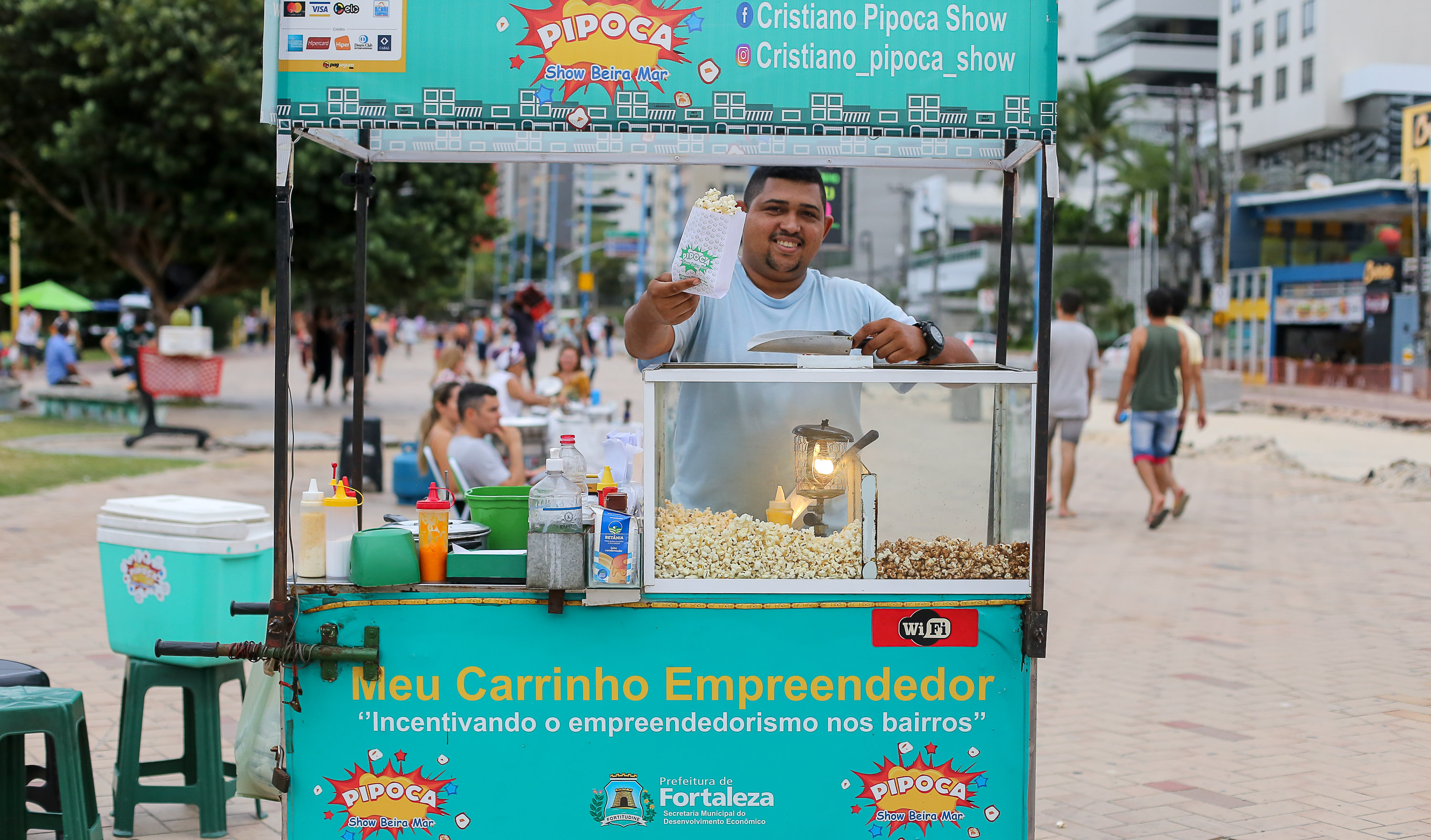 Pipoqueiro em carrinho segurando saco de pipocas