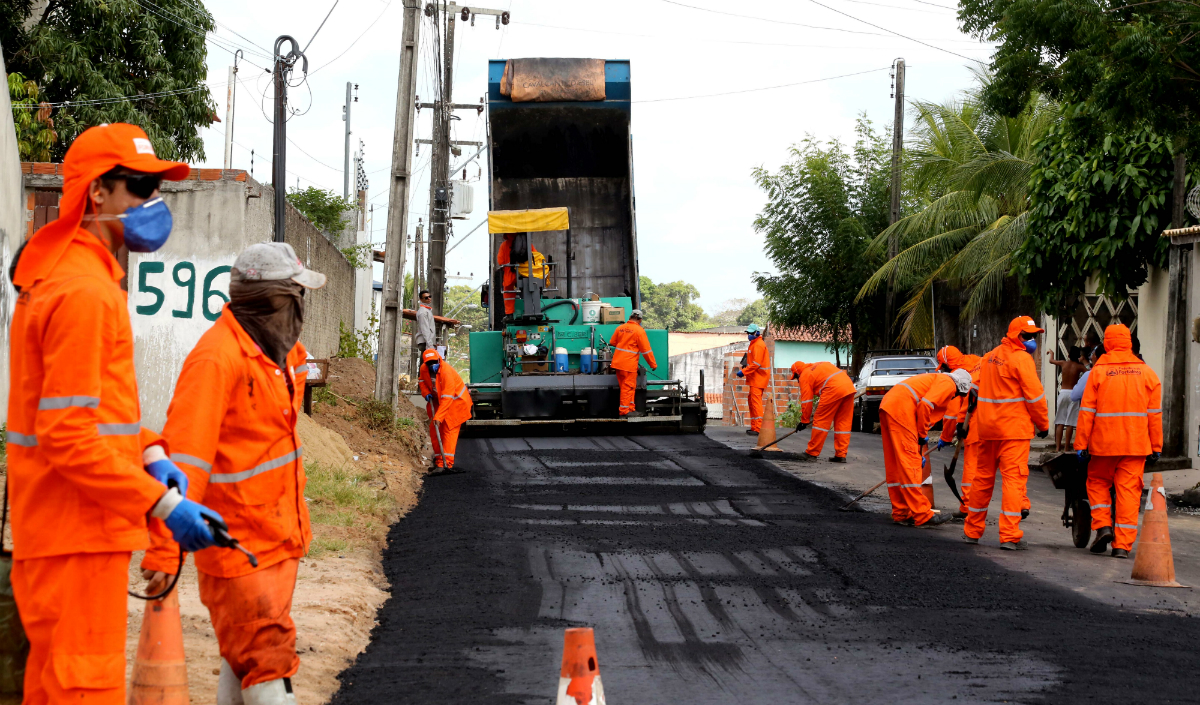 Muitos homens trabalhando em obra no asfalto com caminhão ao fundo