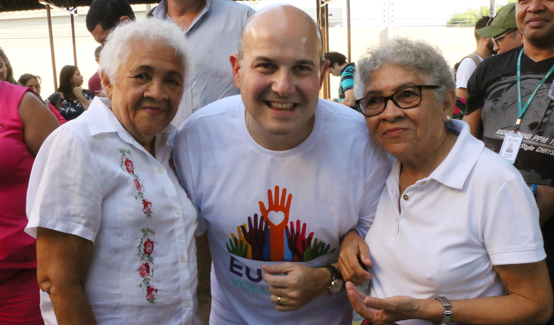 Prefeito entre duas senhoras idosas sorrindo para a foto