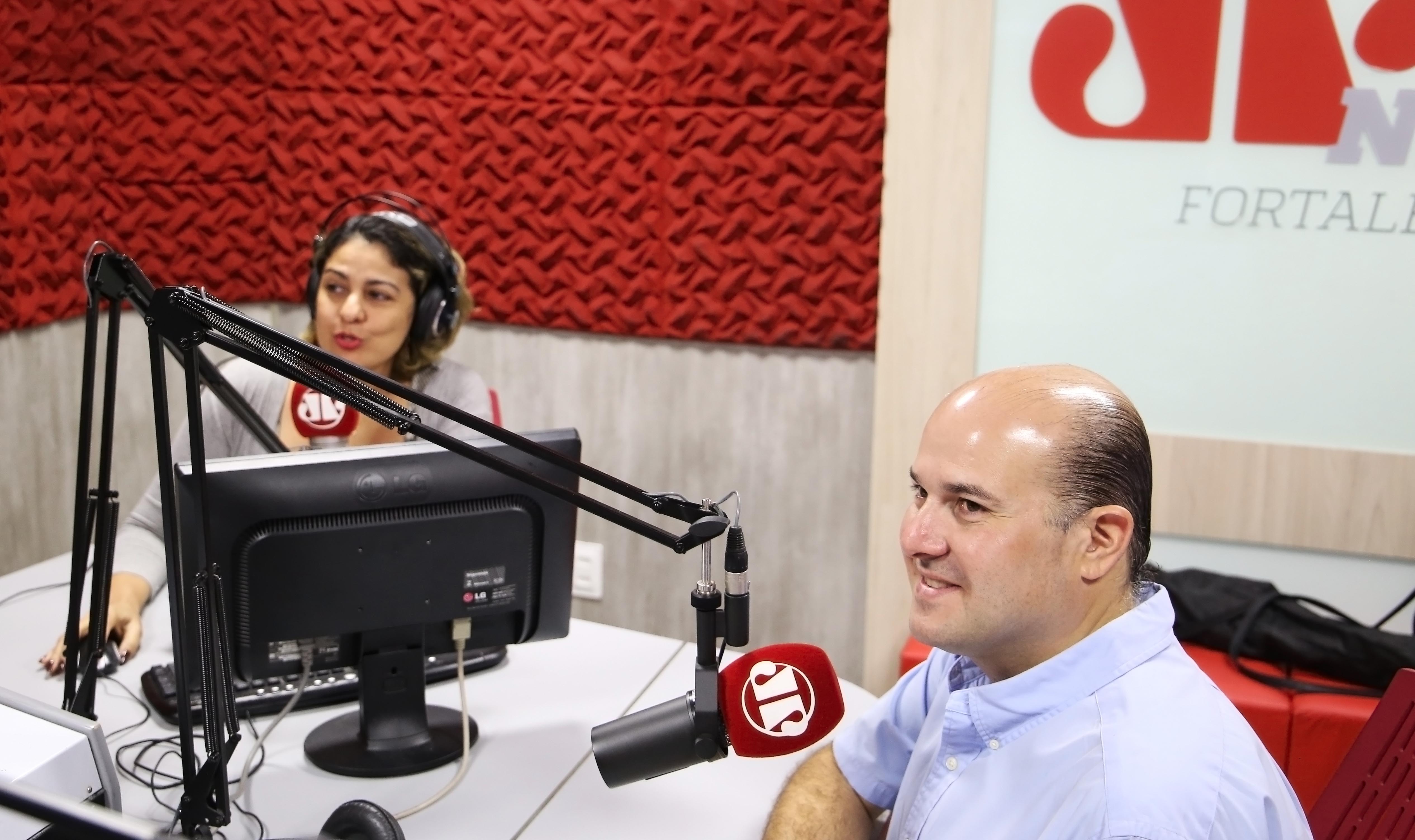 Prefeito e apresentadora em estúdio de rádio sentados conversando ao microfone