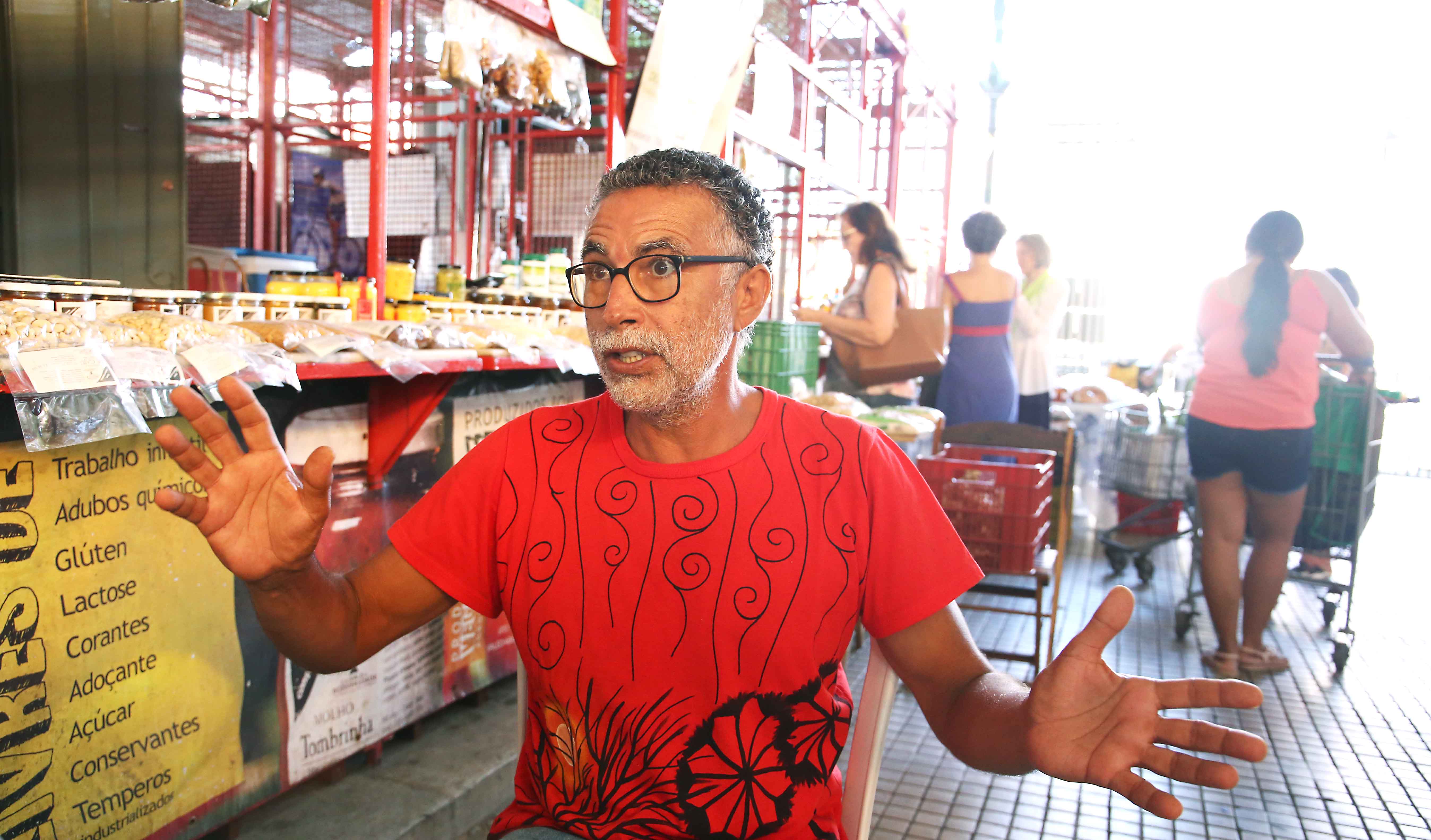 Homem de óculos sentado falando com braços abertos