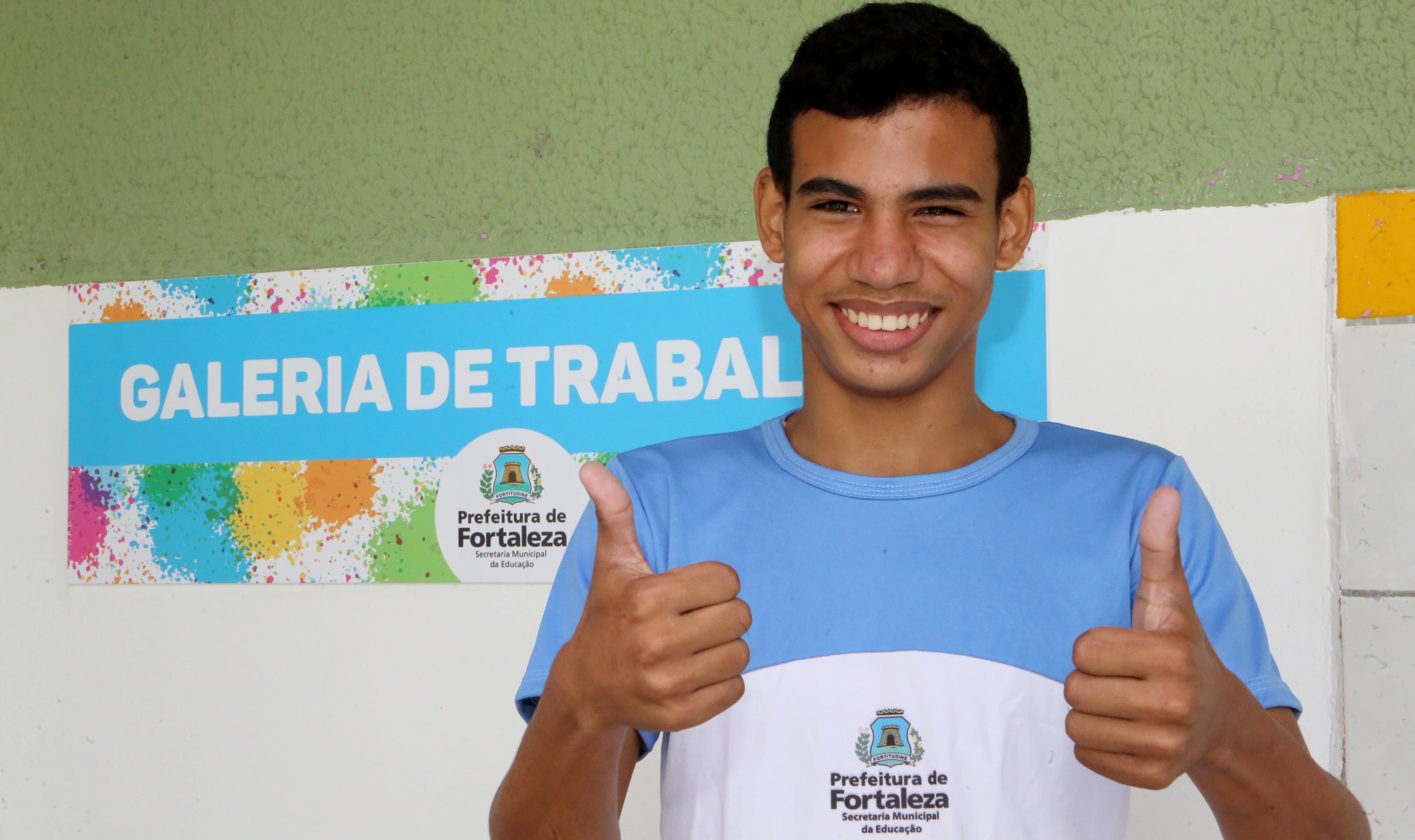 Garoto sorrindo para a foto e fazendo sinal de positivo com as mãos