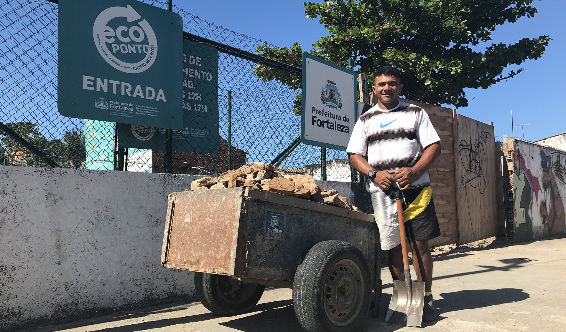 Homem sorrindo ao lado de carrinho com entulhos