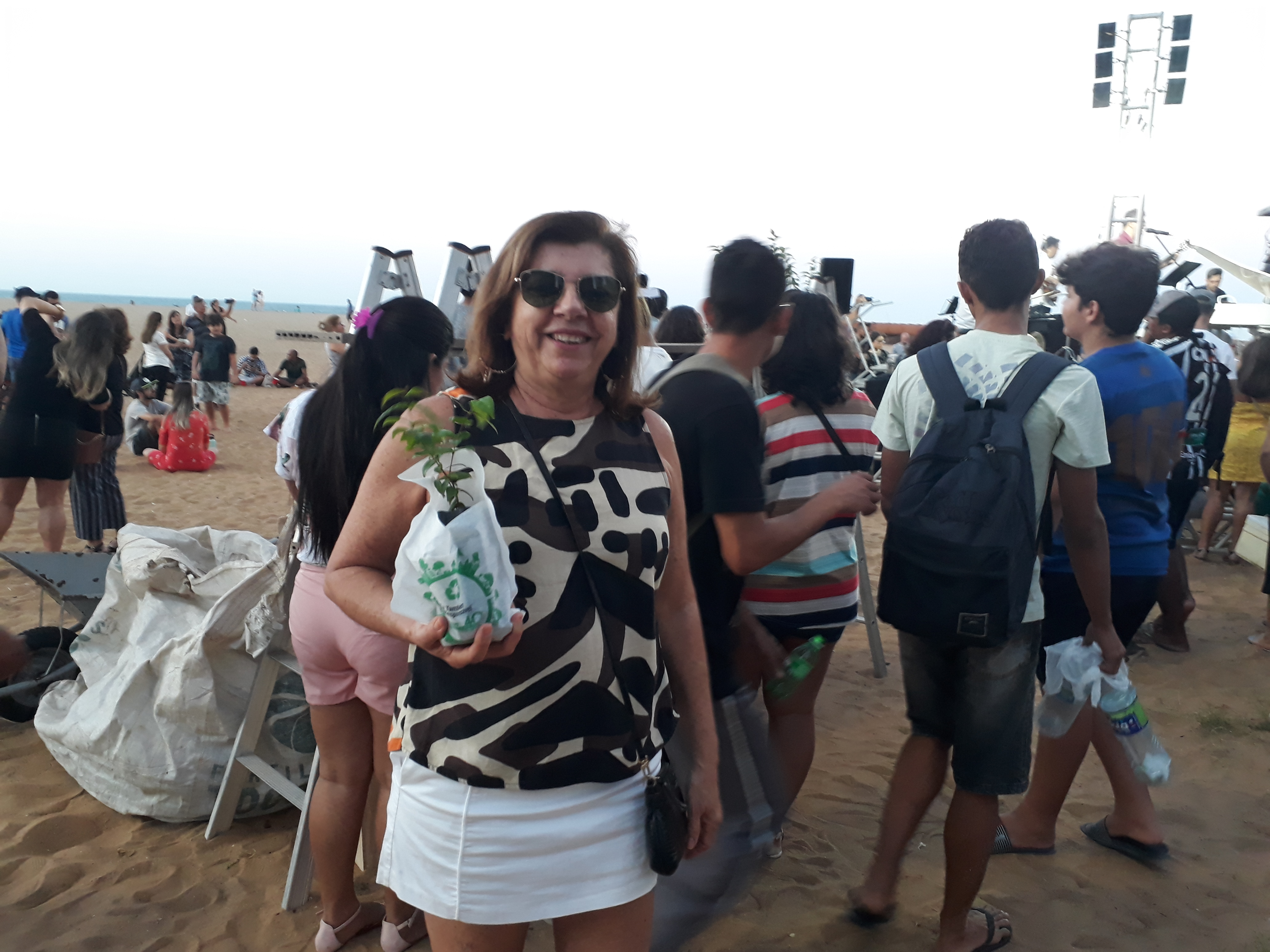 Mulher de óculos escurdos sorrindo e segurando muda de planta