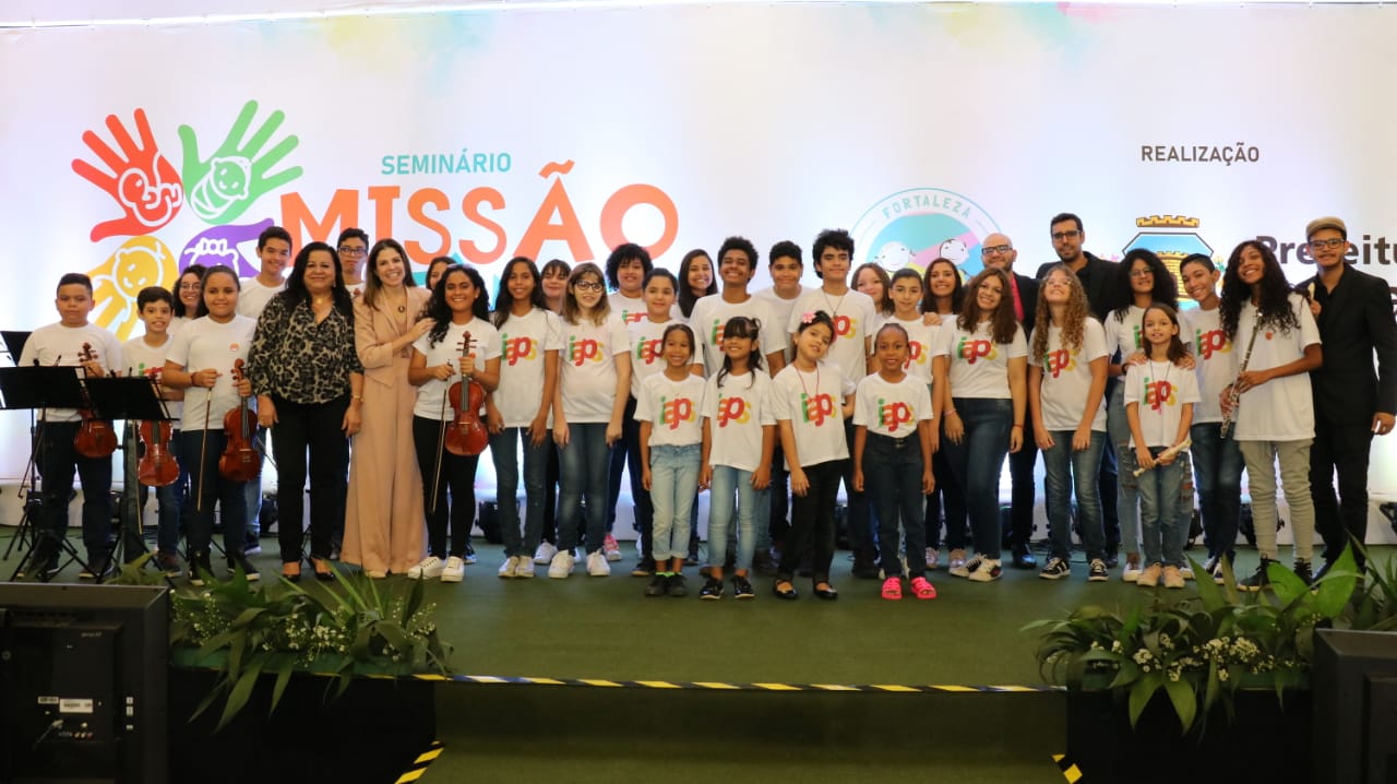 Primeira-dama em cima de palco ao lado de crianças da mini-orquestra