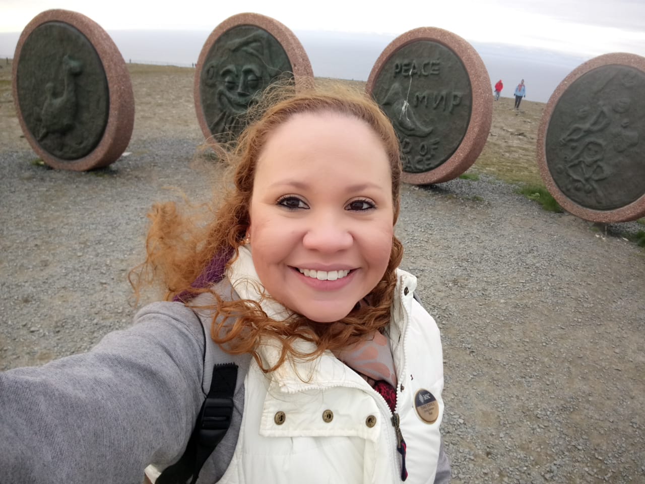 Moça com roupa de frio sorrindo pra foto com monumentos ao fundo