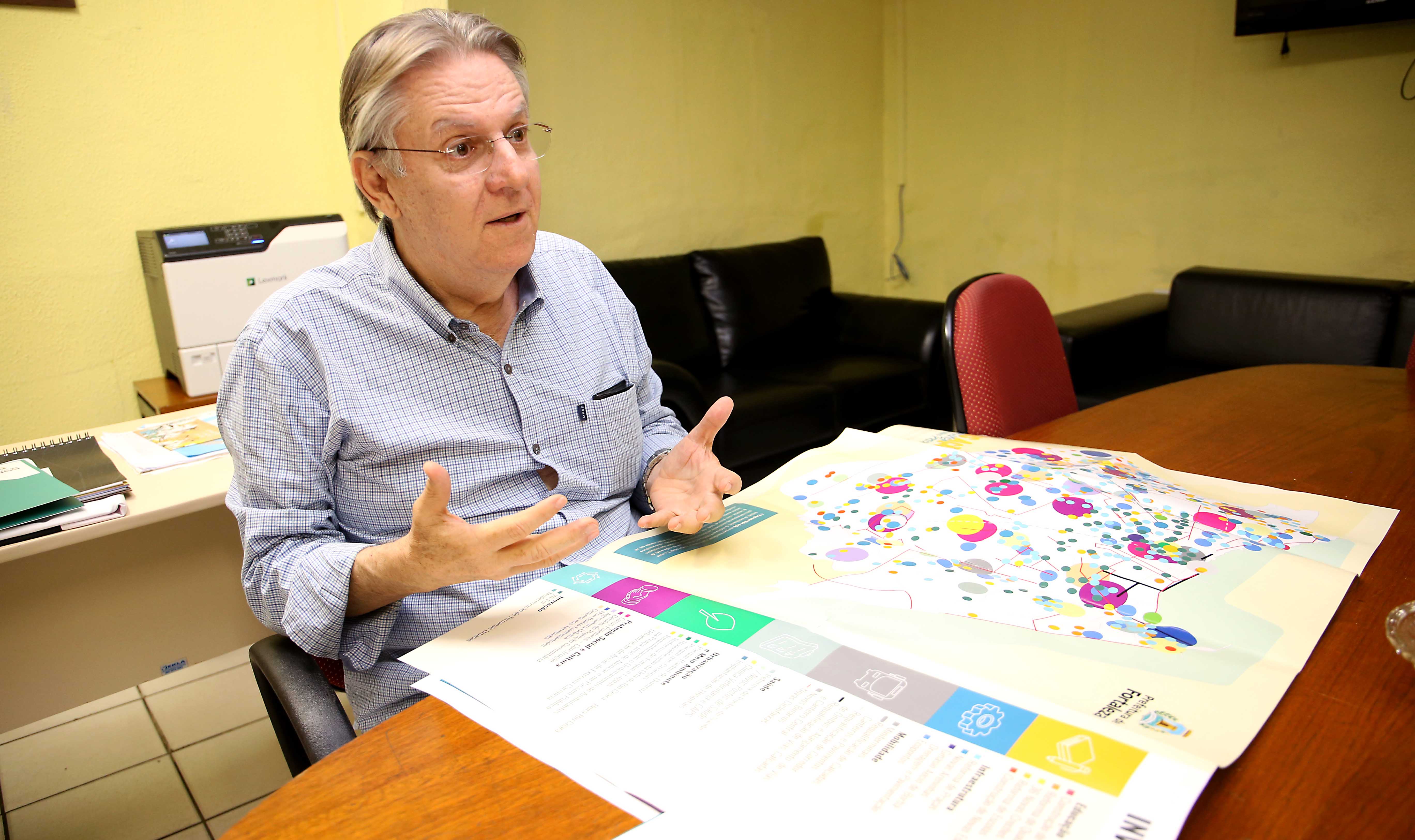 Senhor sentado gesticulando com braços sobre mesa com papéis