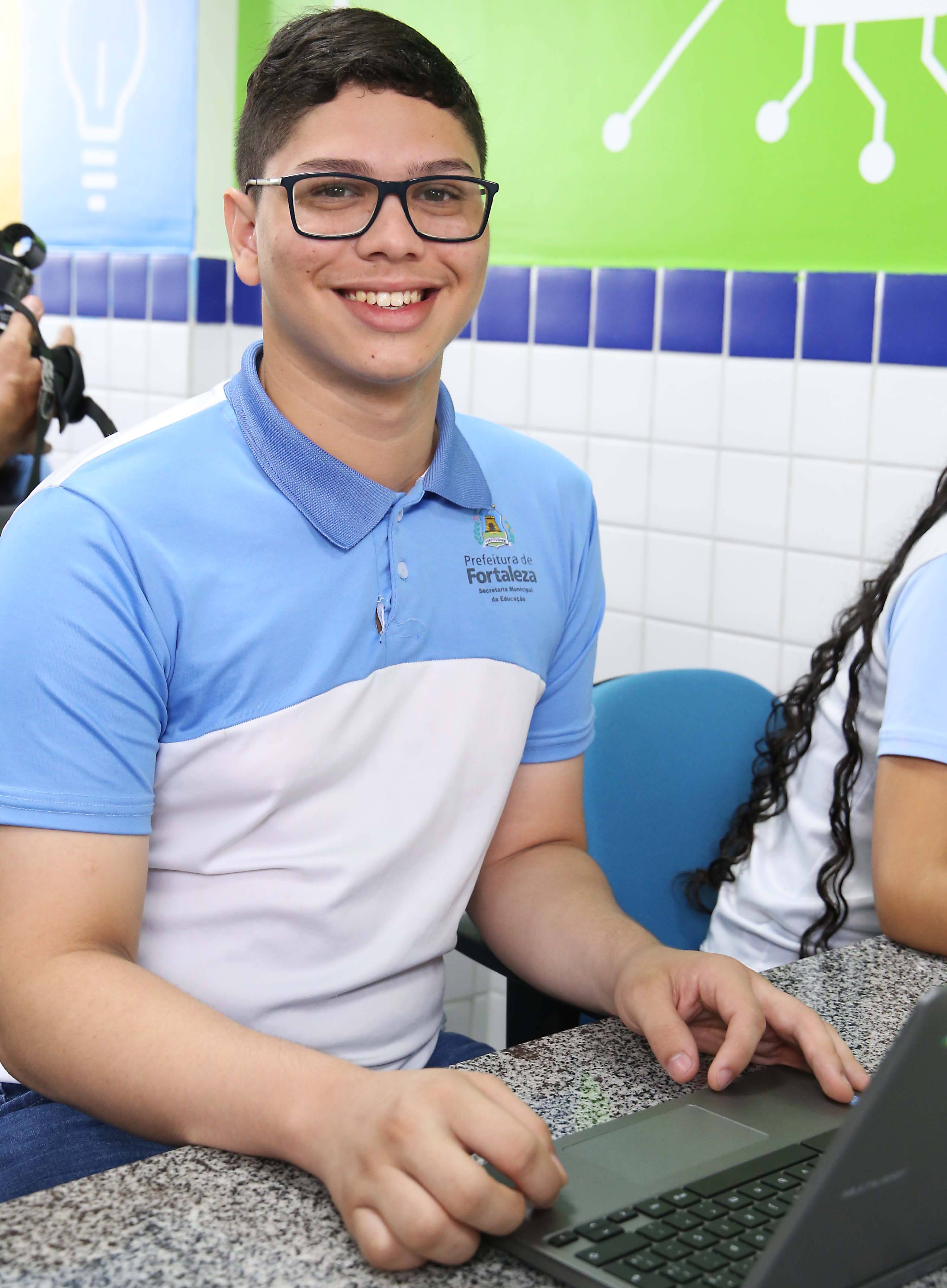 garoto de óculos e farda sorrindo para a foto em frente a computador