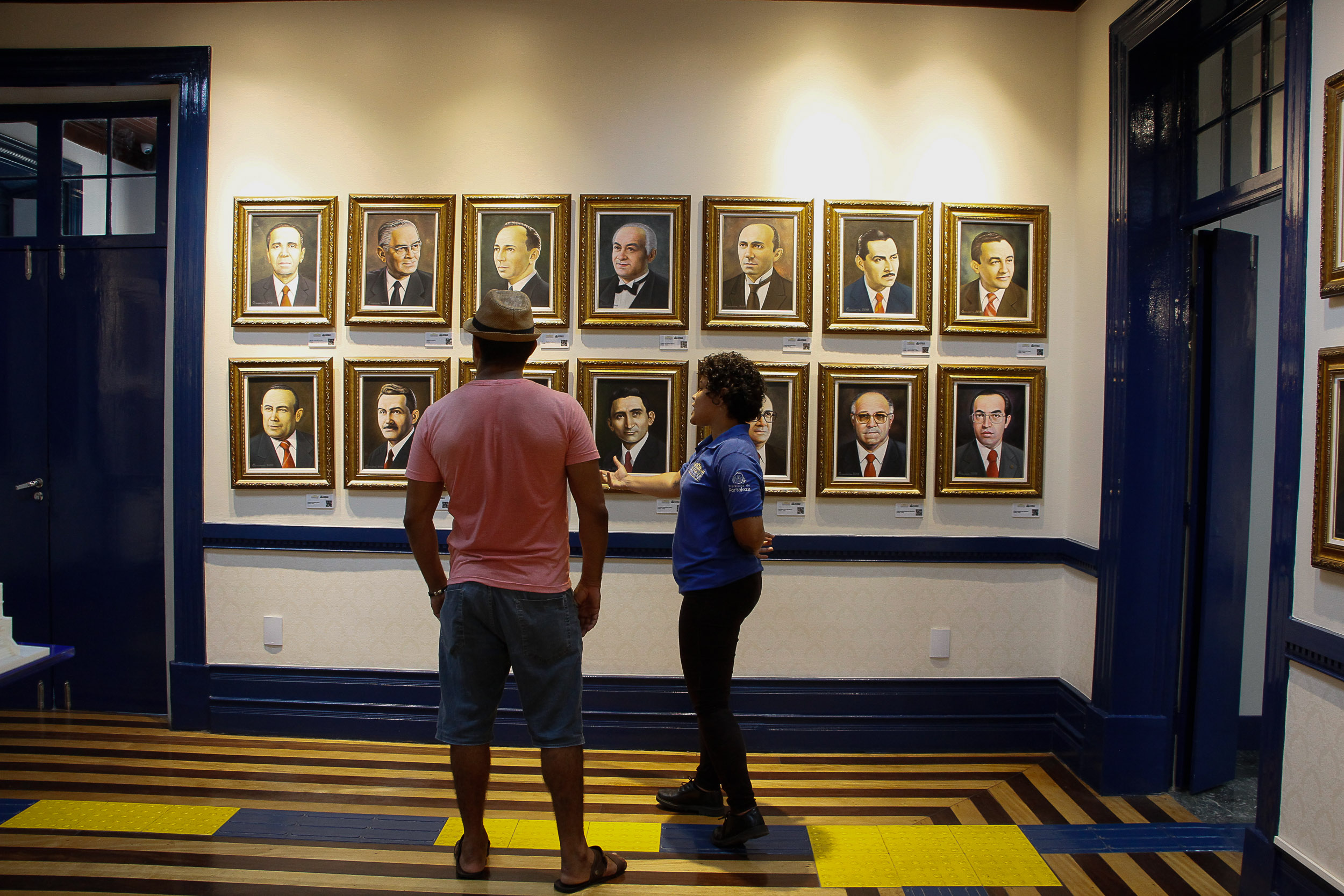 Homem observa exposição no Memorial do Paço enquanto monitora realiza visita guiada