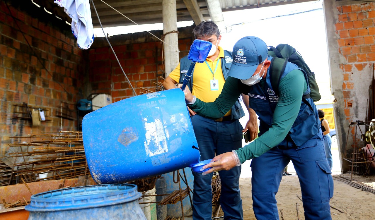 agentes de saúde examinam um balde num quintal