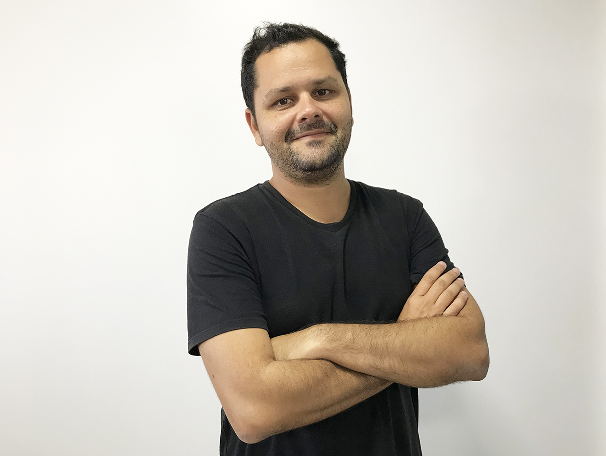 Davi Gomes de camiseta com braços cruzados sorrindo para a foto em fundo branco