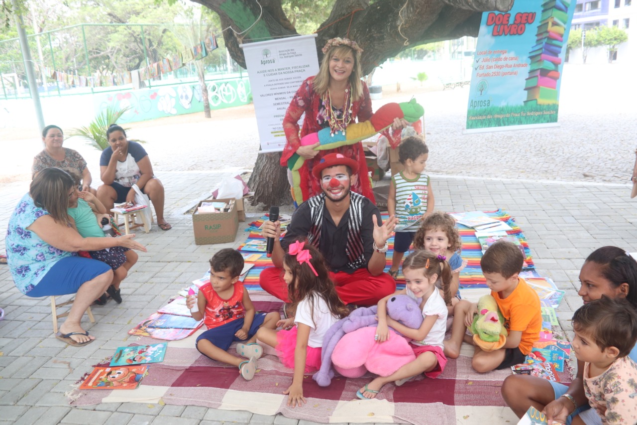 crianças, mulher e palhaço em frente ao quiosque de leitura sorrindo para a foto