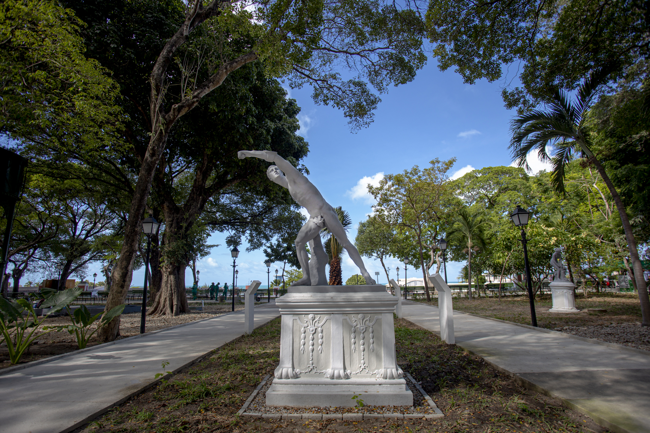 estátua de homem nu no meio com bancos e árvores ao redor