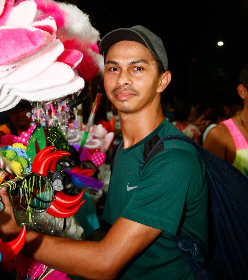 rapaz de lado segurando acessórios de carnaval olhando para a câmera