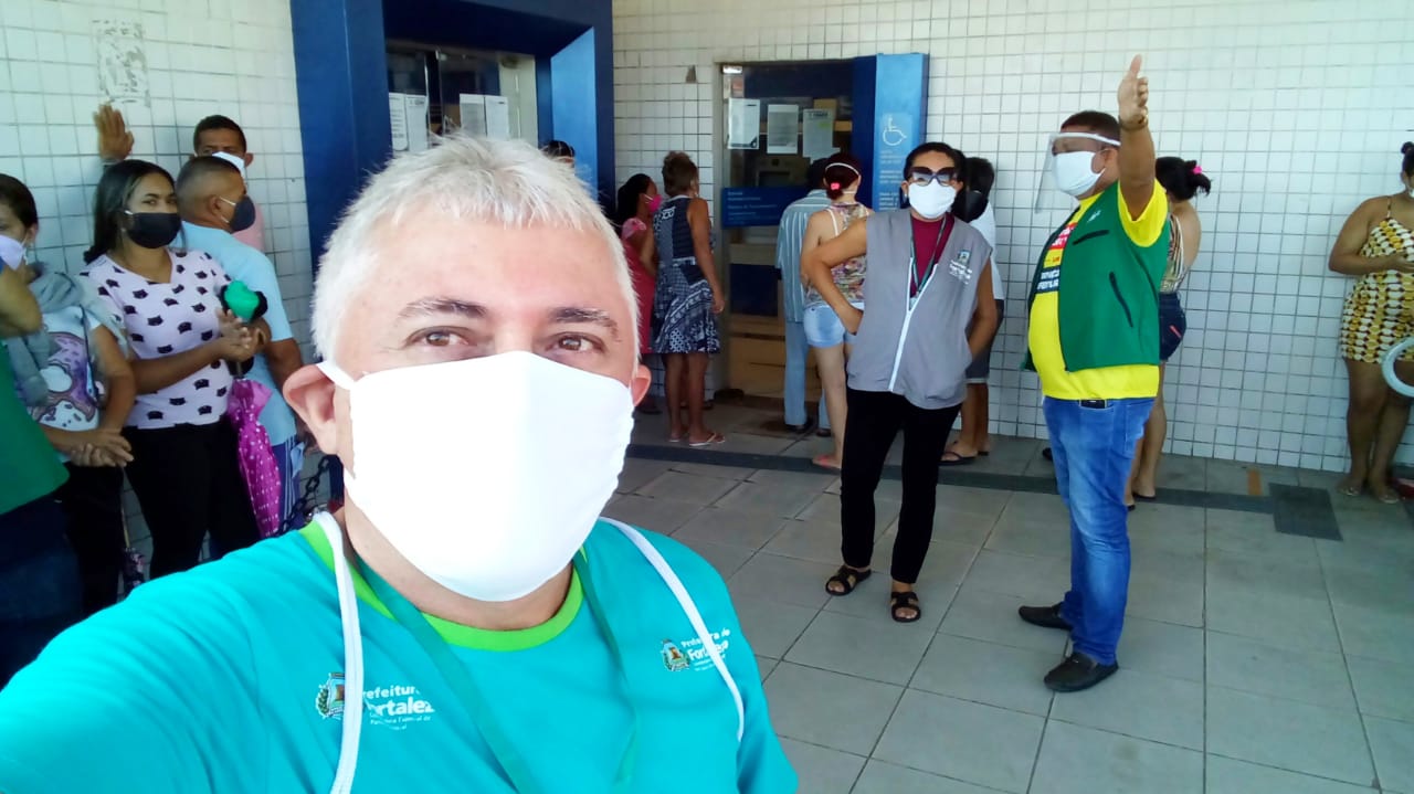 senhor de máscara posando para a foto com pessoas em fila ao fundo