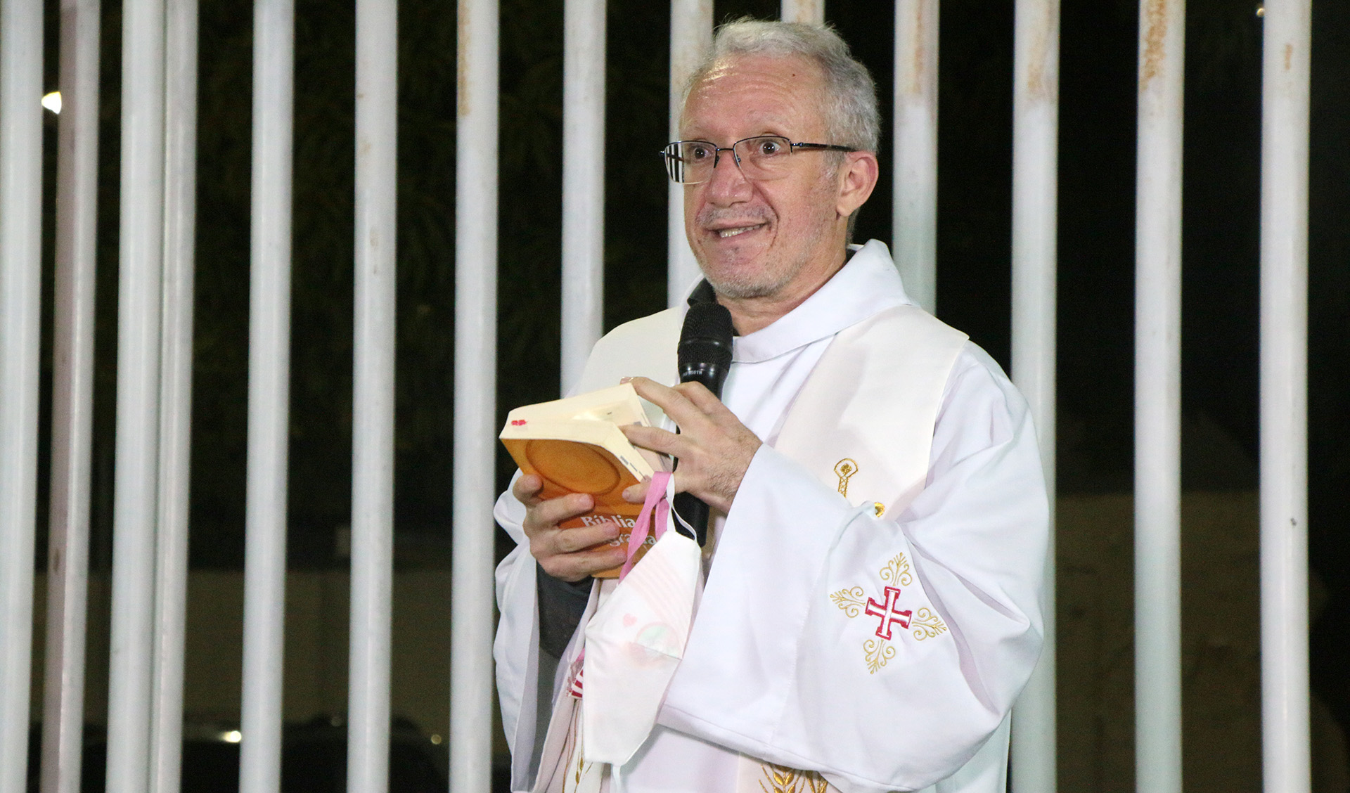 padre falando ao microfone e segurando bíblica