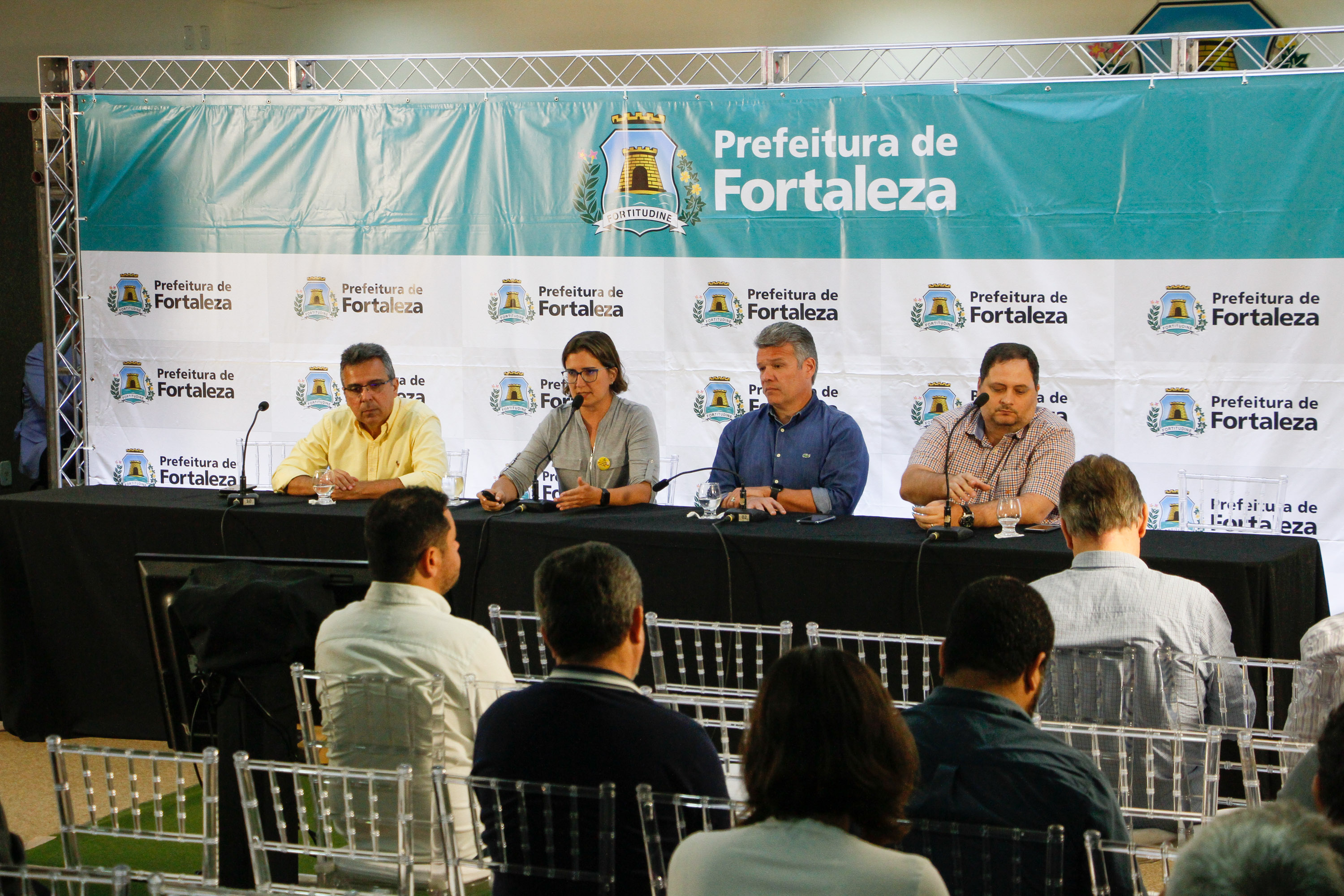 secretários sentados à mesa com painel da prefeitura ao fundo