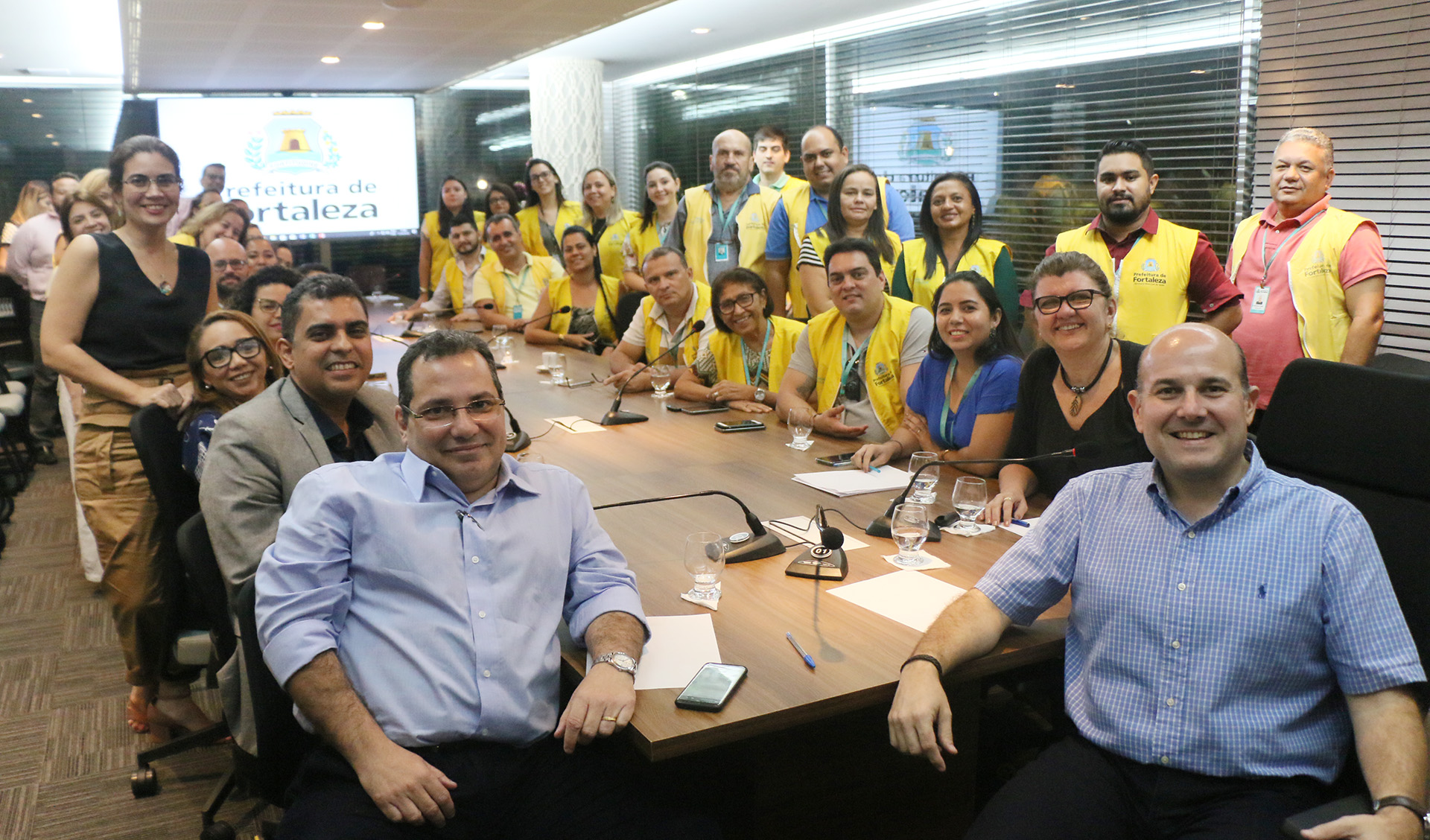 Prefeito e pessoas sentados ao redor de mesa sorrindo para a foto