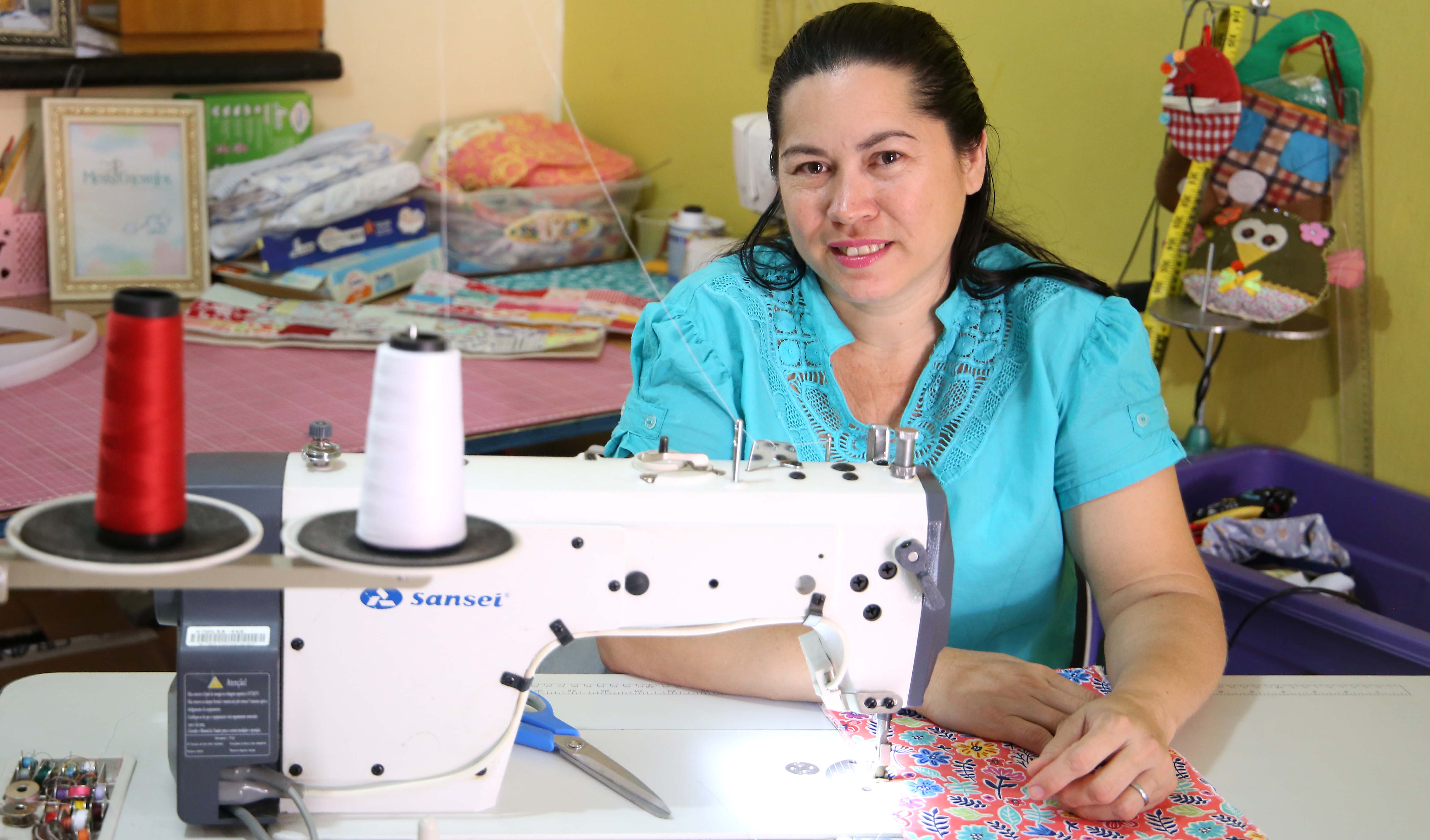 senhora sentada usando máquina de costura e posando pra foto