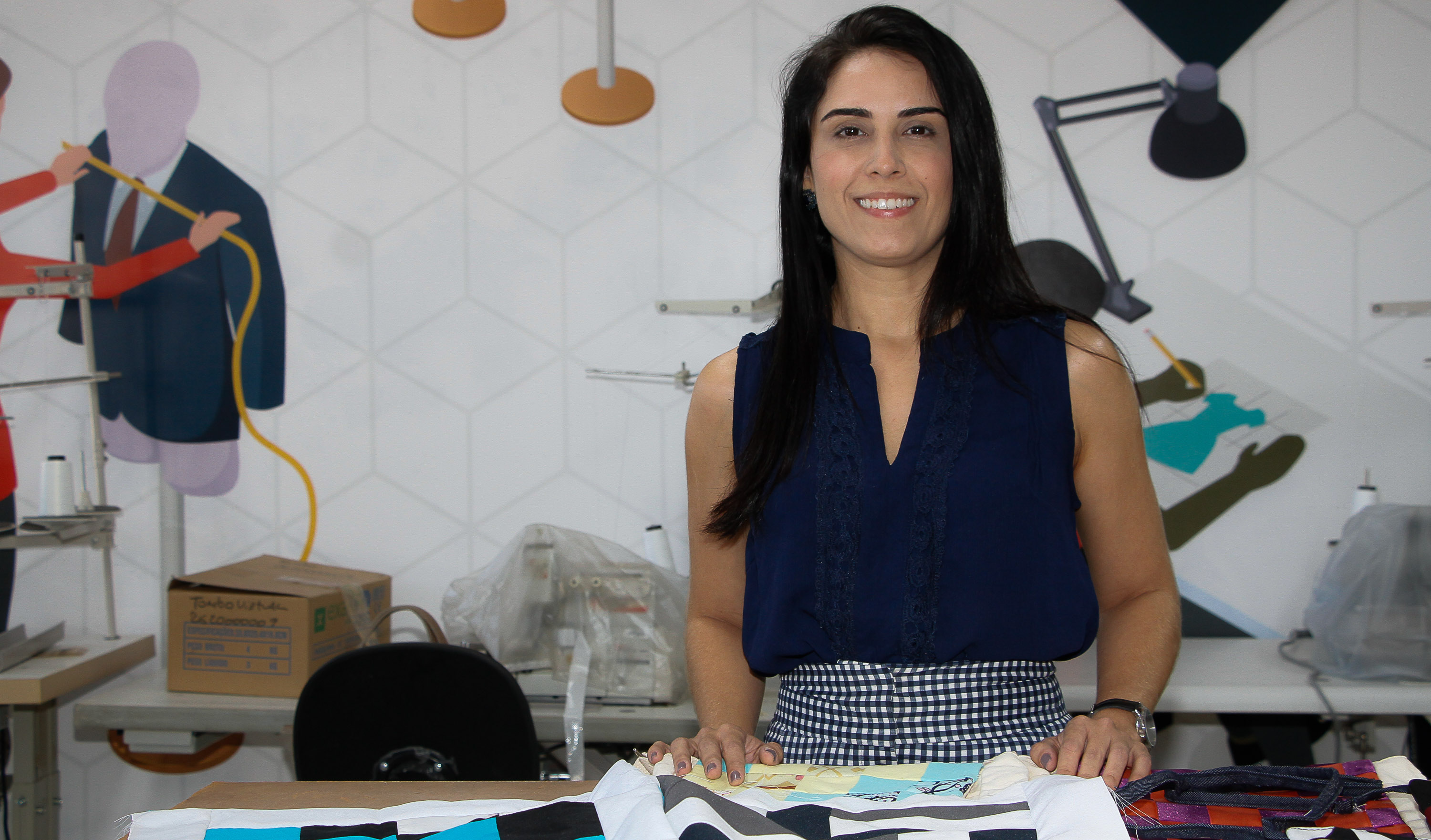 mulher sorrindo para a foto em frente à mesa com tecidos em cima