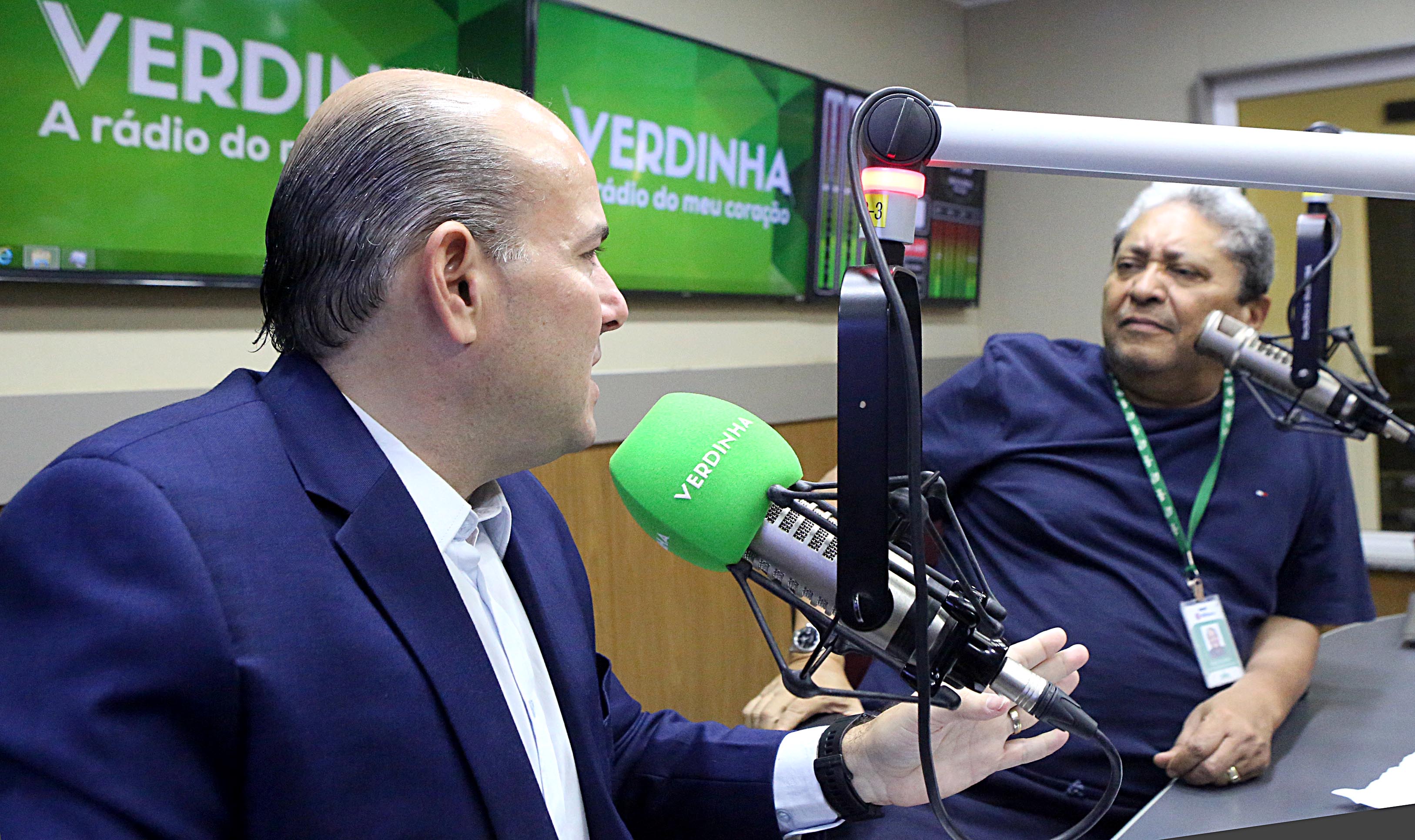 prefeito falando ao microfone em estúdio de rádio e radialista ao lado olhando