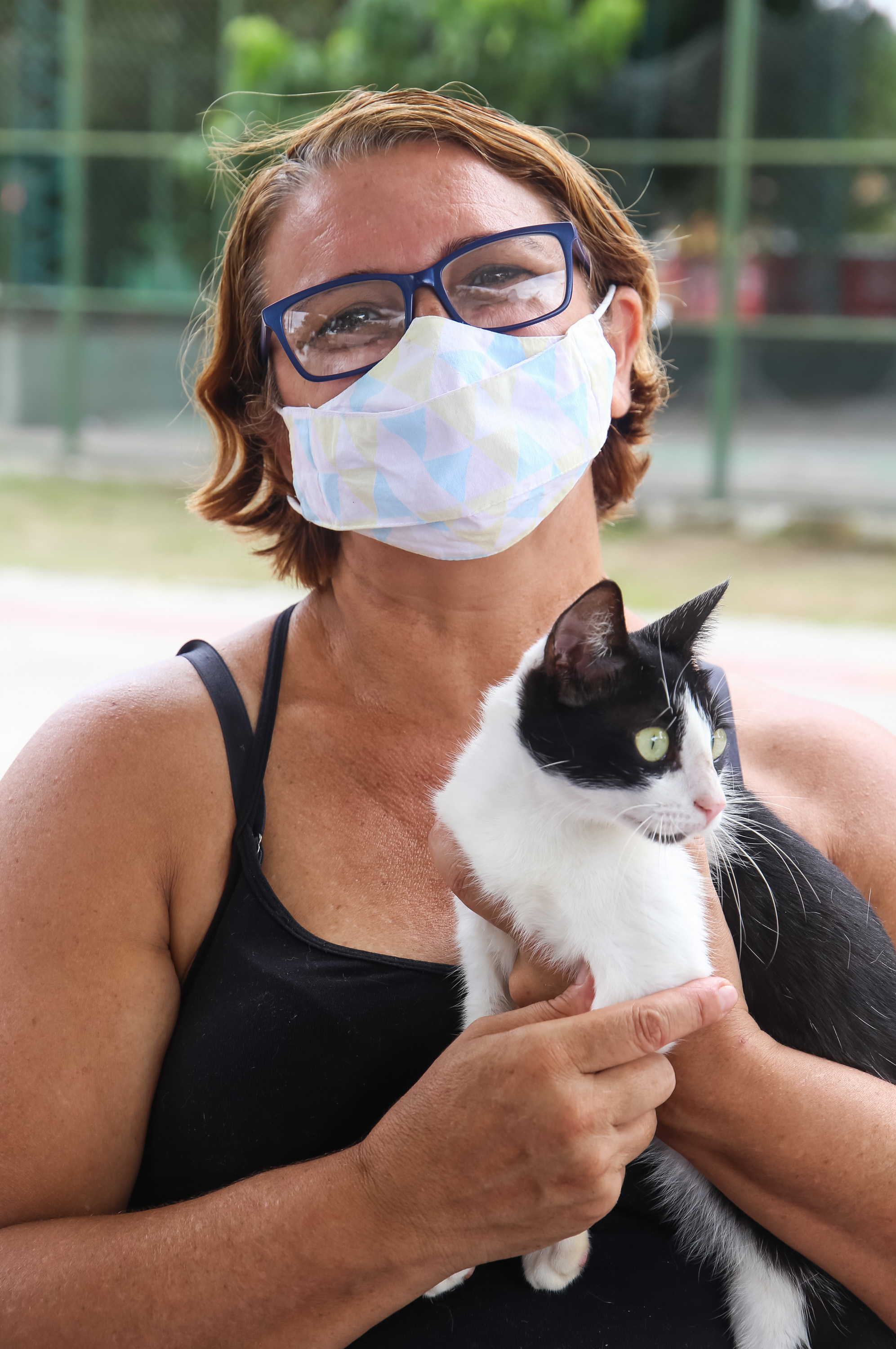 Mulher de máscara e com blusa cor de preta segura gato nos braços. 