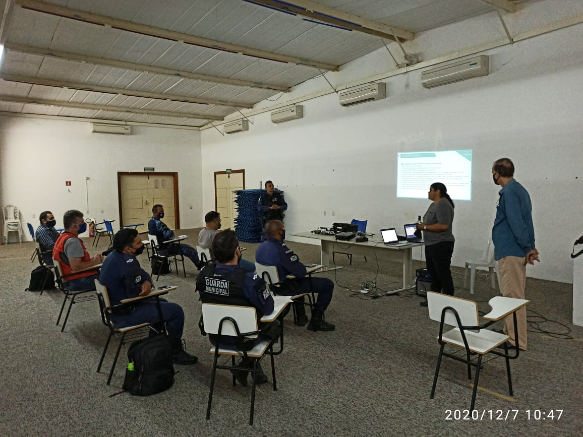 pessoas sentadas em salada de aula de frente para quadro com duas pessoas na frente em pé falando