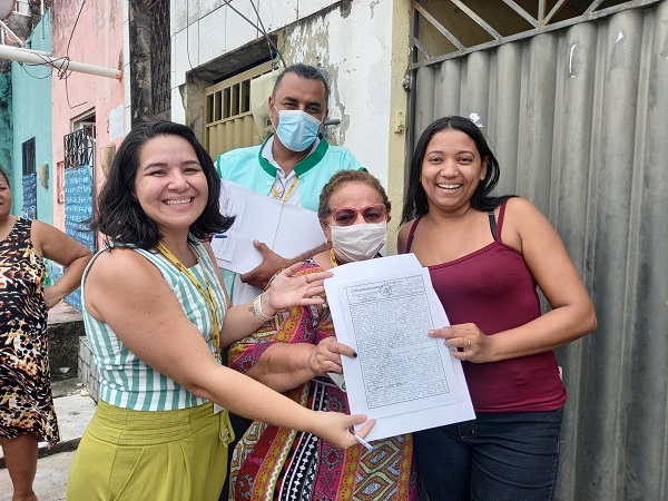 Funcionários da Habitafor entregam papel da casa para moradora